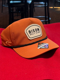 Orange cap with 'Bison Golf Club' logo on a red surface in a bar setting