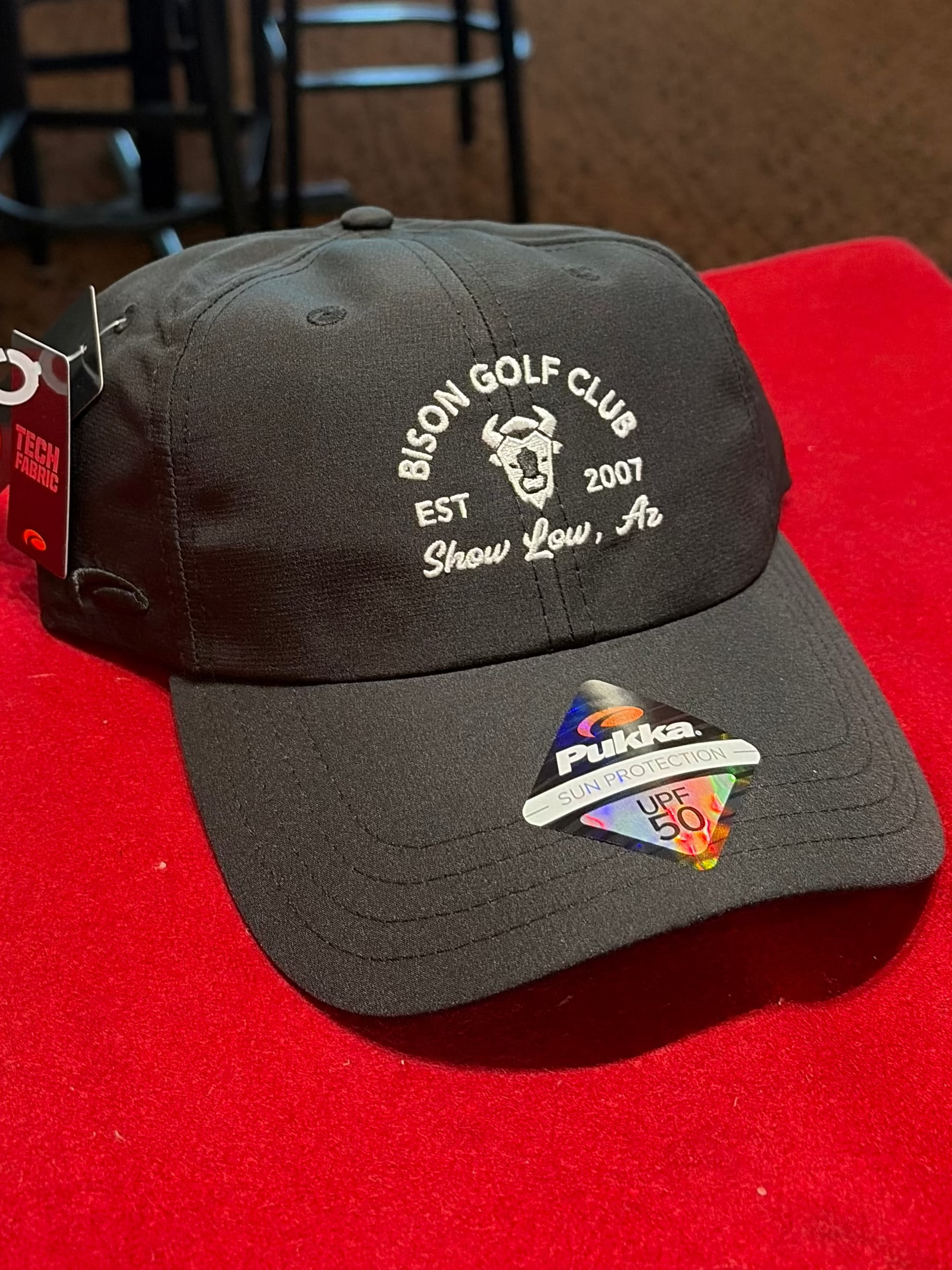 Black cap with branding on a red surface, with a bar setting in the background